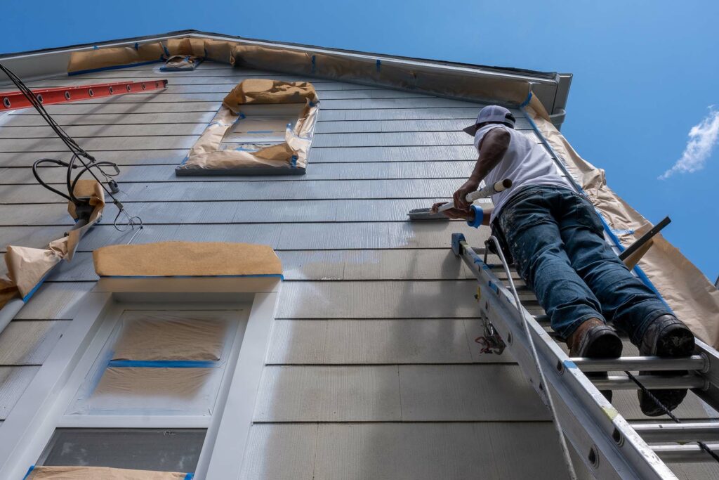 Painter on a ladder rolling paint onto the exterior of a house