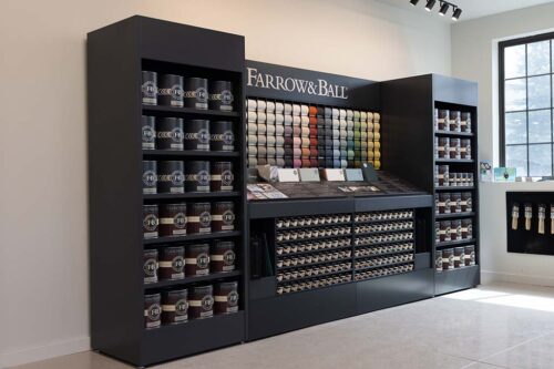 Farrow & Ball paint display in a paint supply store, featuring paint cans, a color sample wall, and shelves with various paint options.