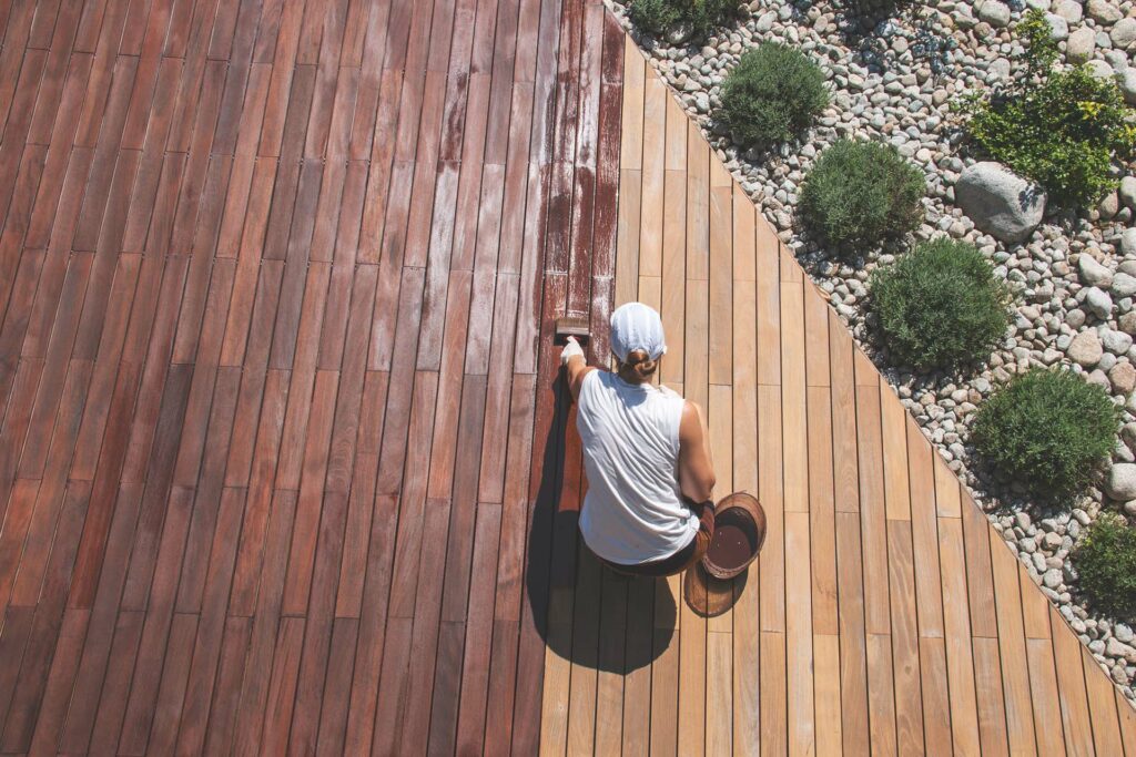 Wood deck renovation treatment, the person applying protective wood stain with a brush.